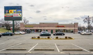 Exterior view of a strip mall with cars parked in front.
