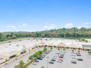 Aerial view of a shopping center with parking lot and surrounding trees.