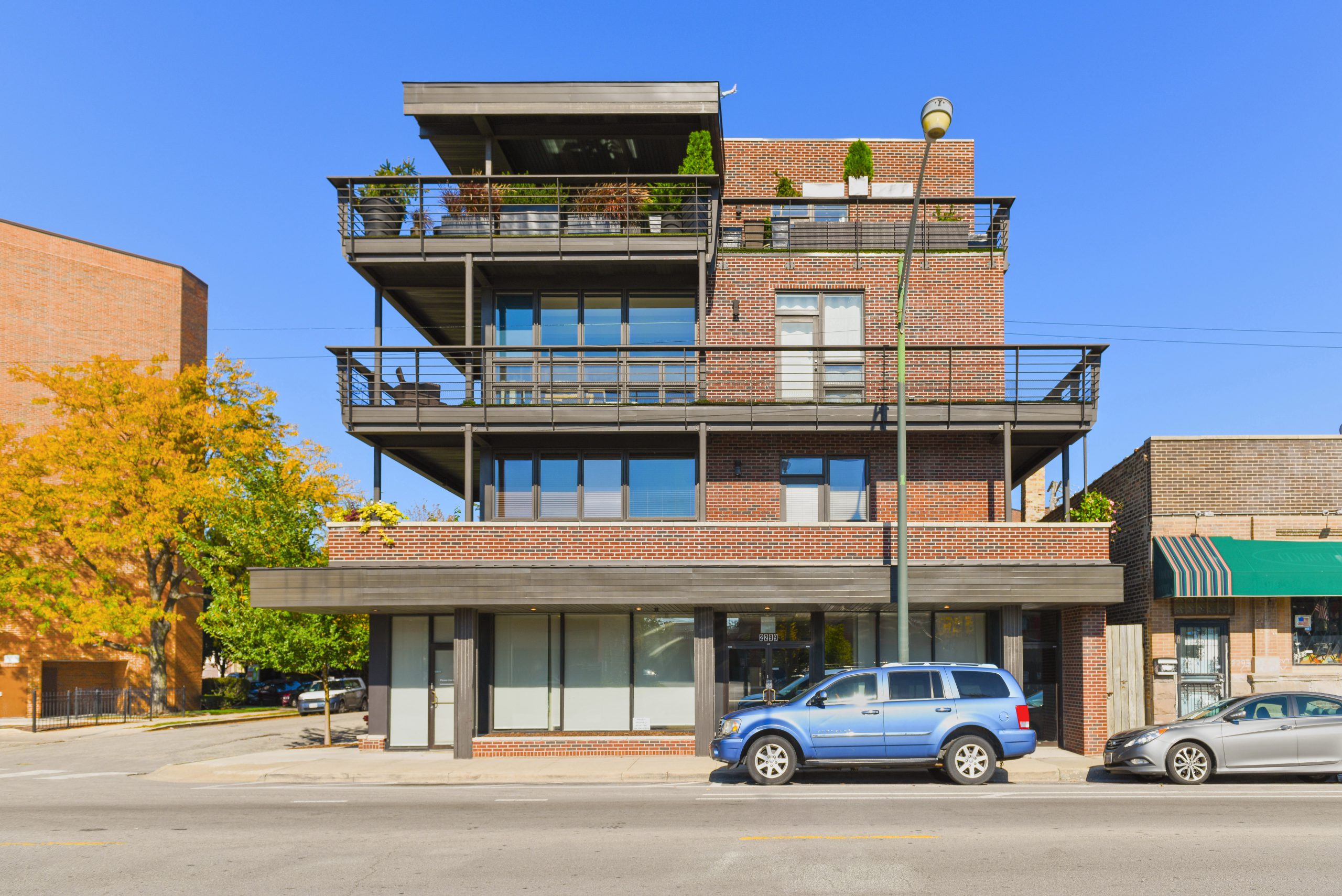 Three-story brick building with balconies and a blue SUV parked in front.
