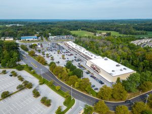 Aerial view of a shopping center with parking lot and surrounding greenery.