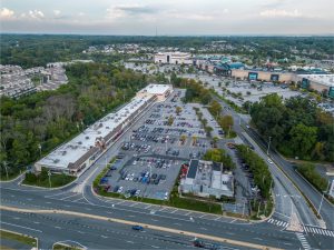 Aerial view of a shopping center with parking lot and surrounding landscape.
