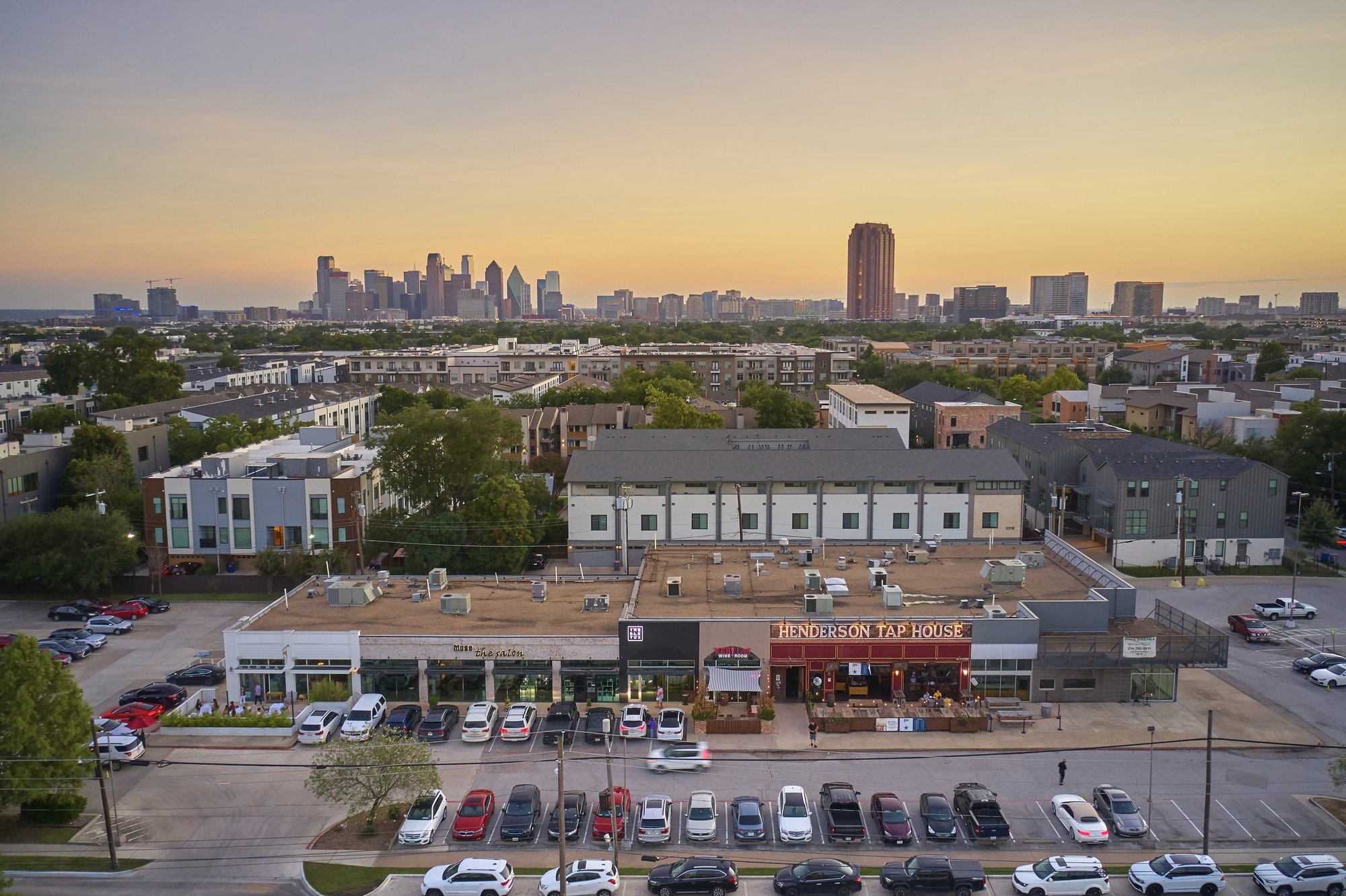 Aerial view of a shopping center and residential area with a city skyline in the background.