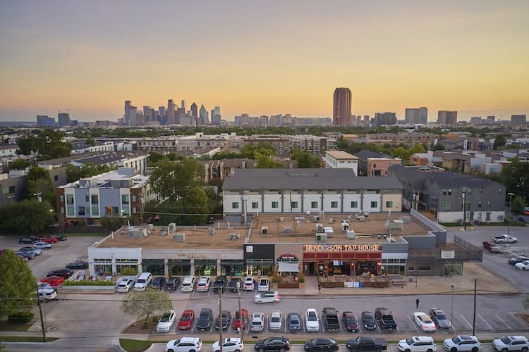 Aerial view of a suburban shopping center with city skyline in the background at sunset.