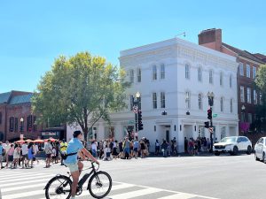 Person on bicycle at busy city intersection with crowd and buildings.