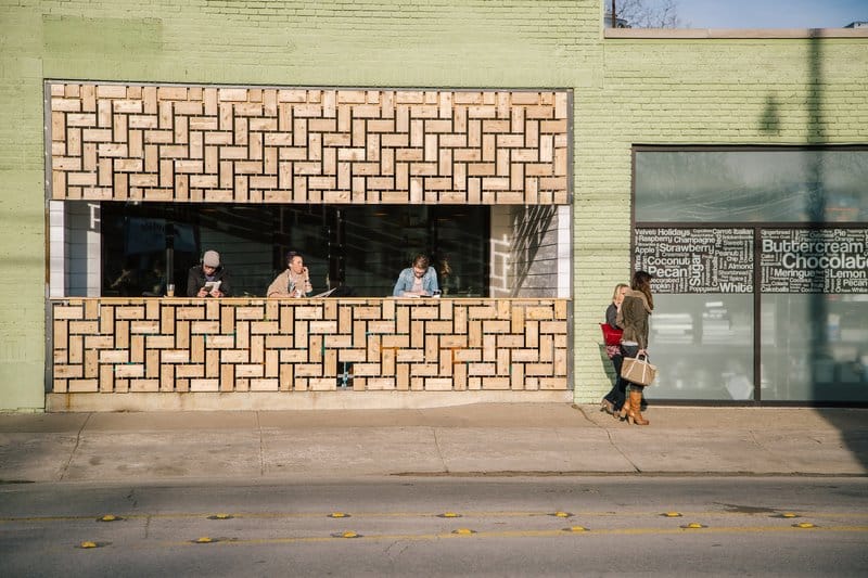 People sitting and standing outside a cafe with a unique brick facade.