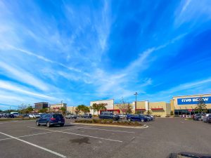 Shopping center parking lot under a bright blue sky.
