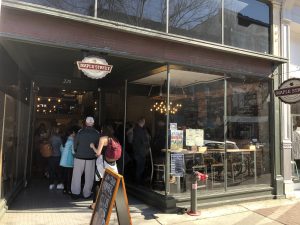 Crowd of people waiting outside a sandwich shop.