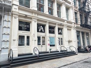 White cast-iron building with three entrances and "Alex Woo" signage.