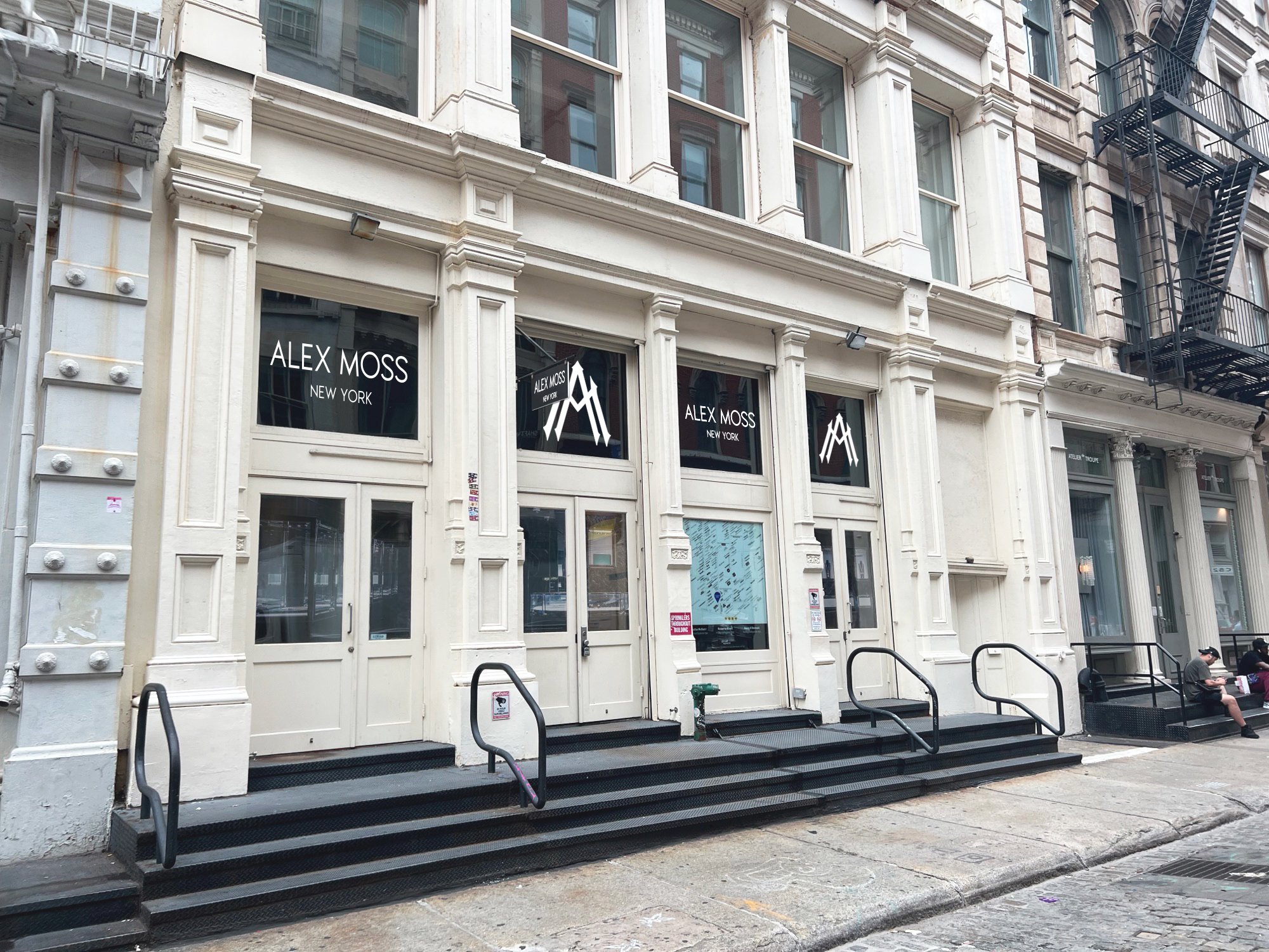 White cast-iron building with three entrances and "Alex Woo" signage.