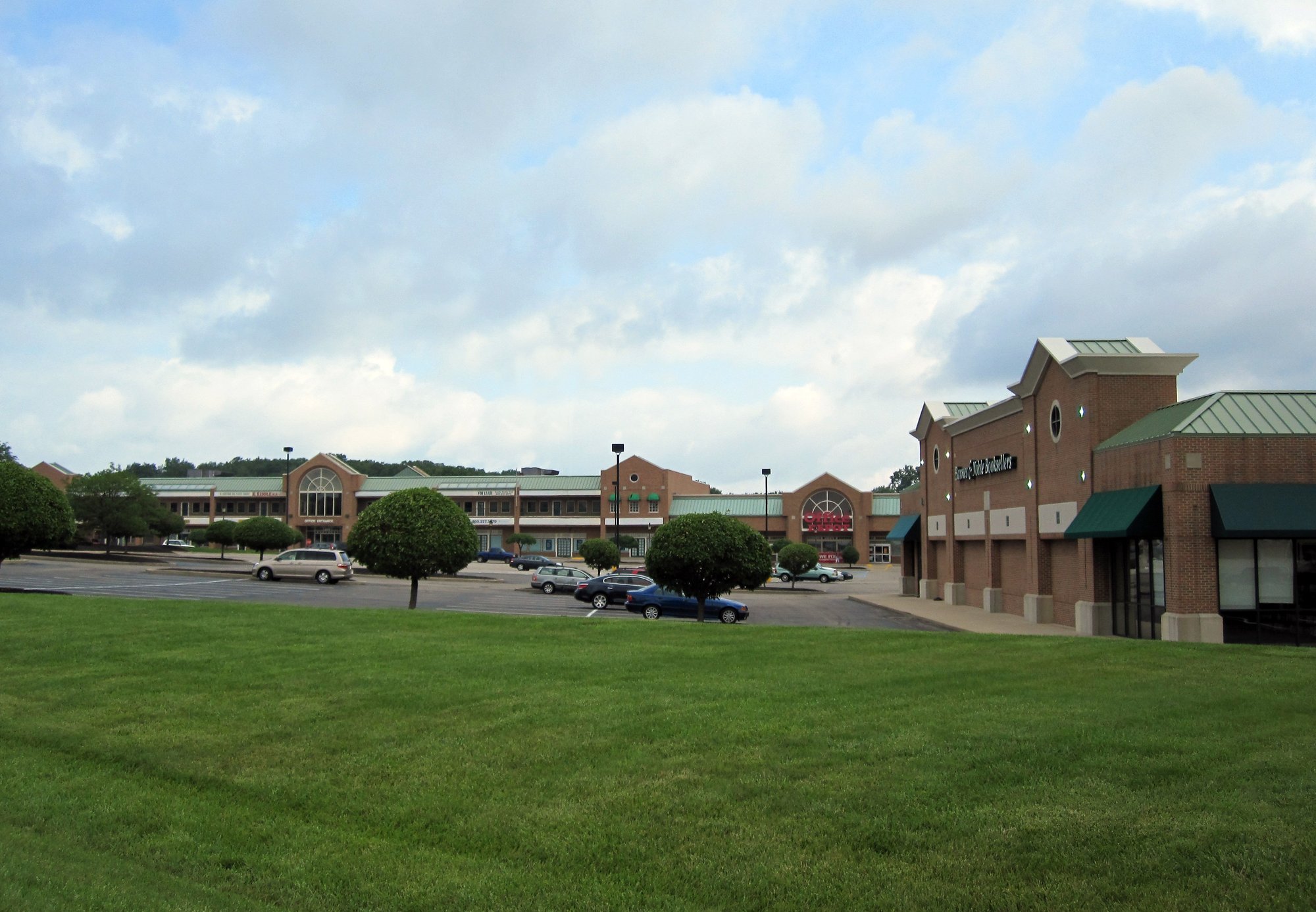 Exterior view of a shopping center with brick buildings and a grassy area.