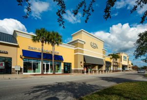 Exterior view of a shopping center with yellow buildings and blue awnings.