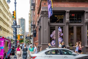 Busy city street corner with pedestrians and a building displaying artwork.