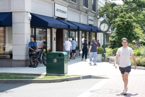 People walking past shops on a sunny street.