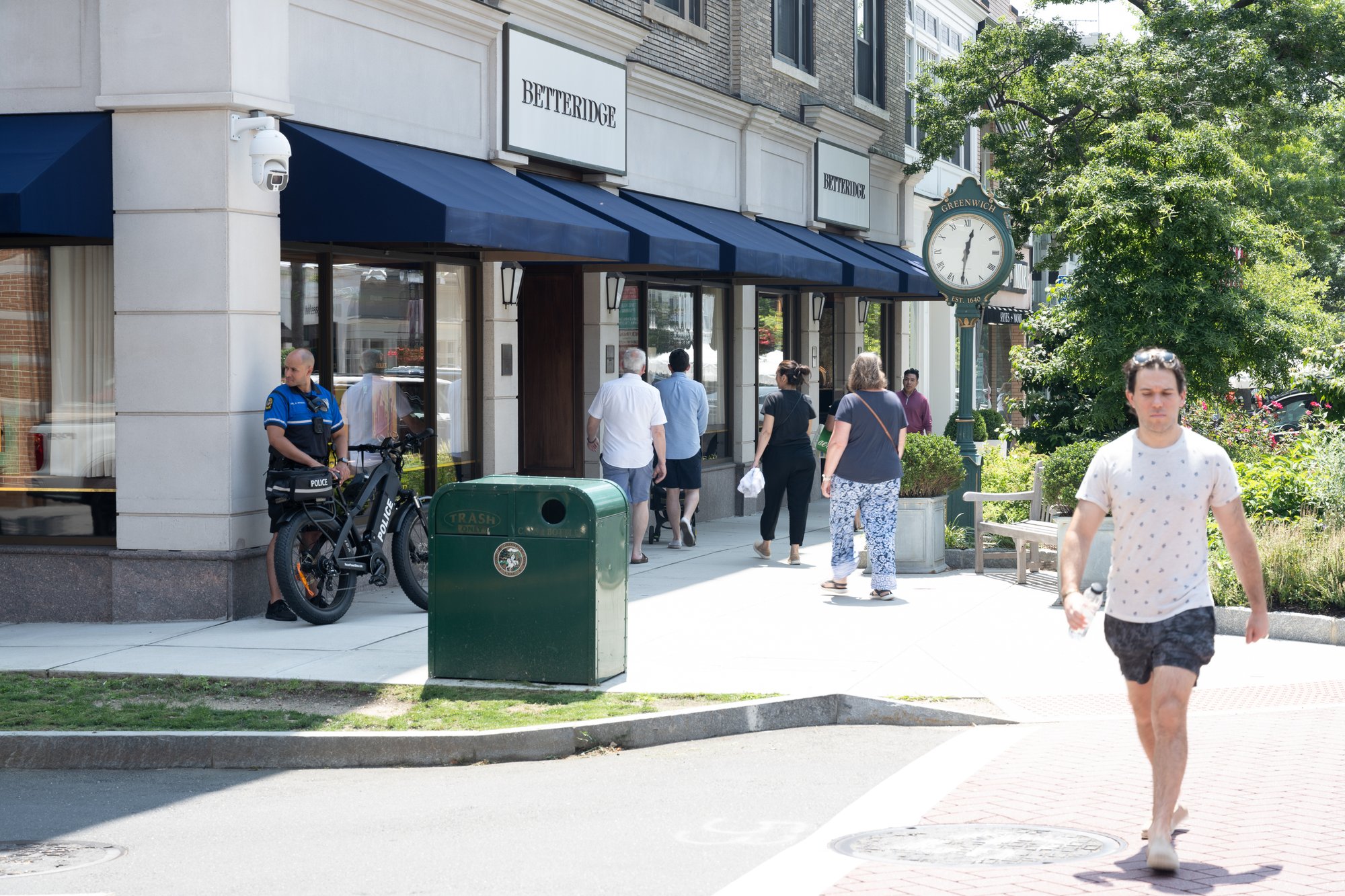 People walking past shops on a sunny street.