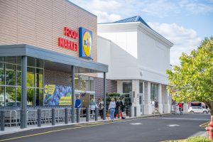 Exterior view of a Lidl grocery store with shoppers waiting outside.