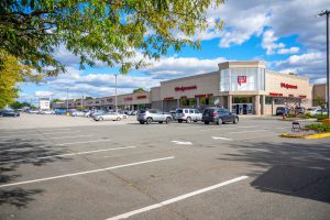 Exterior view of a shopping center parking lot with cars and stores.