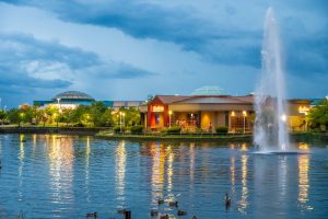 Shopping center at dusk reflected in a pond with fountain.
