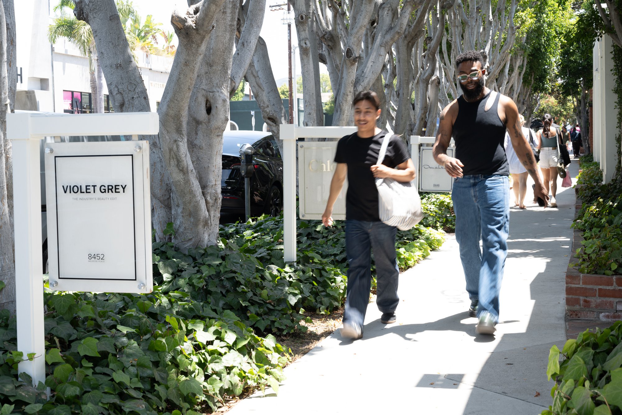 Two men walking down a sidewalk lined with trees.
