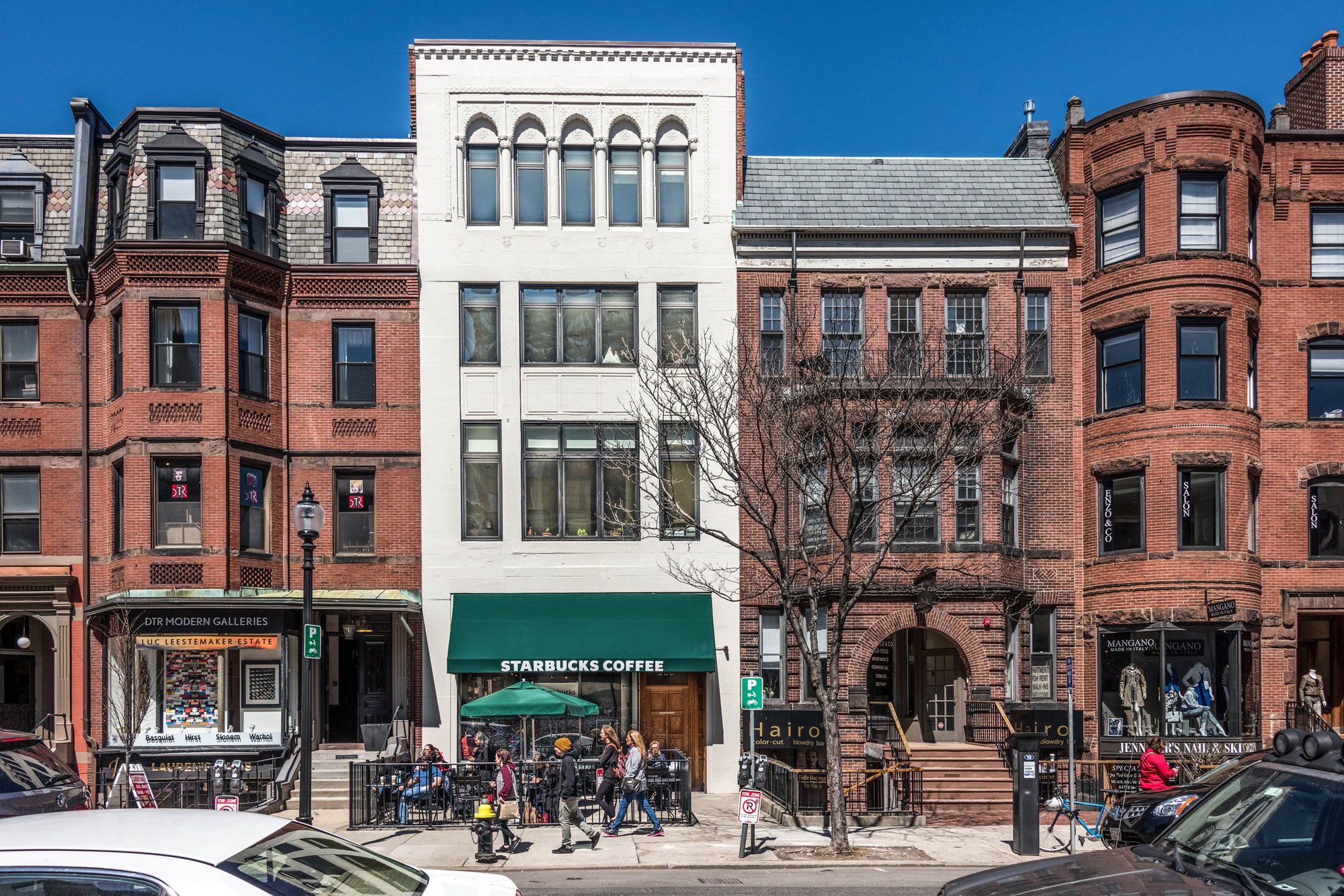 Three-story white building with green awning between brick buildings on a city street.