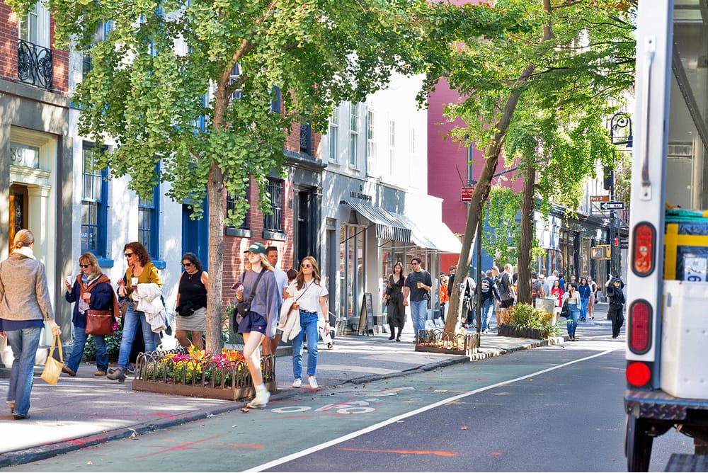 People shopping and walking on a tree-lined street.