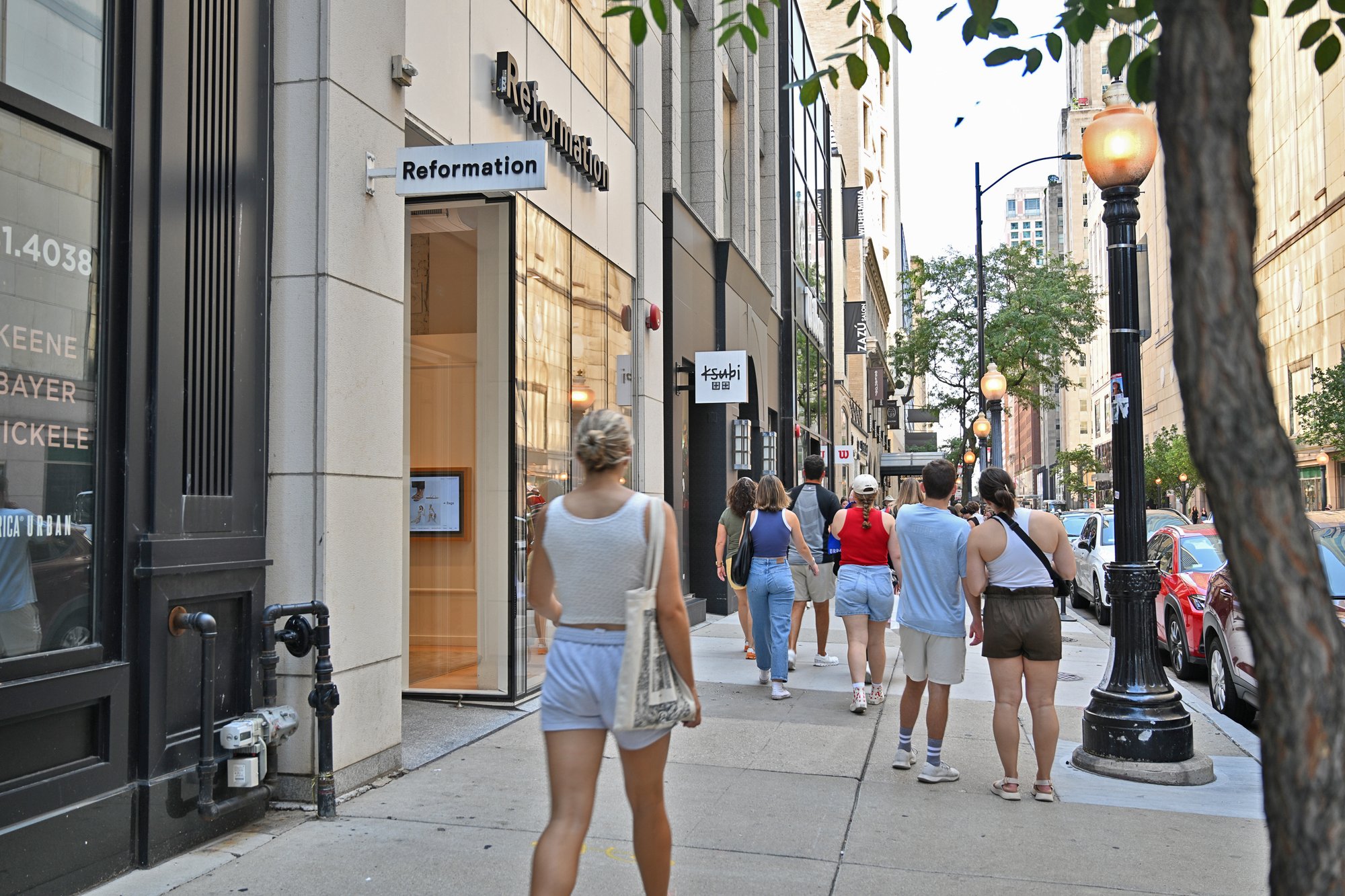 People walking down a city sidewalk past a boutique storefront.