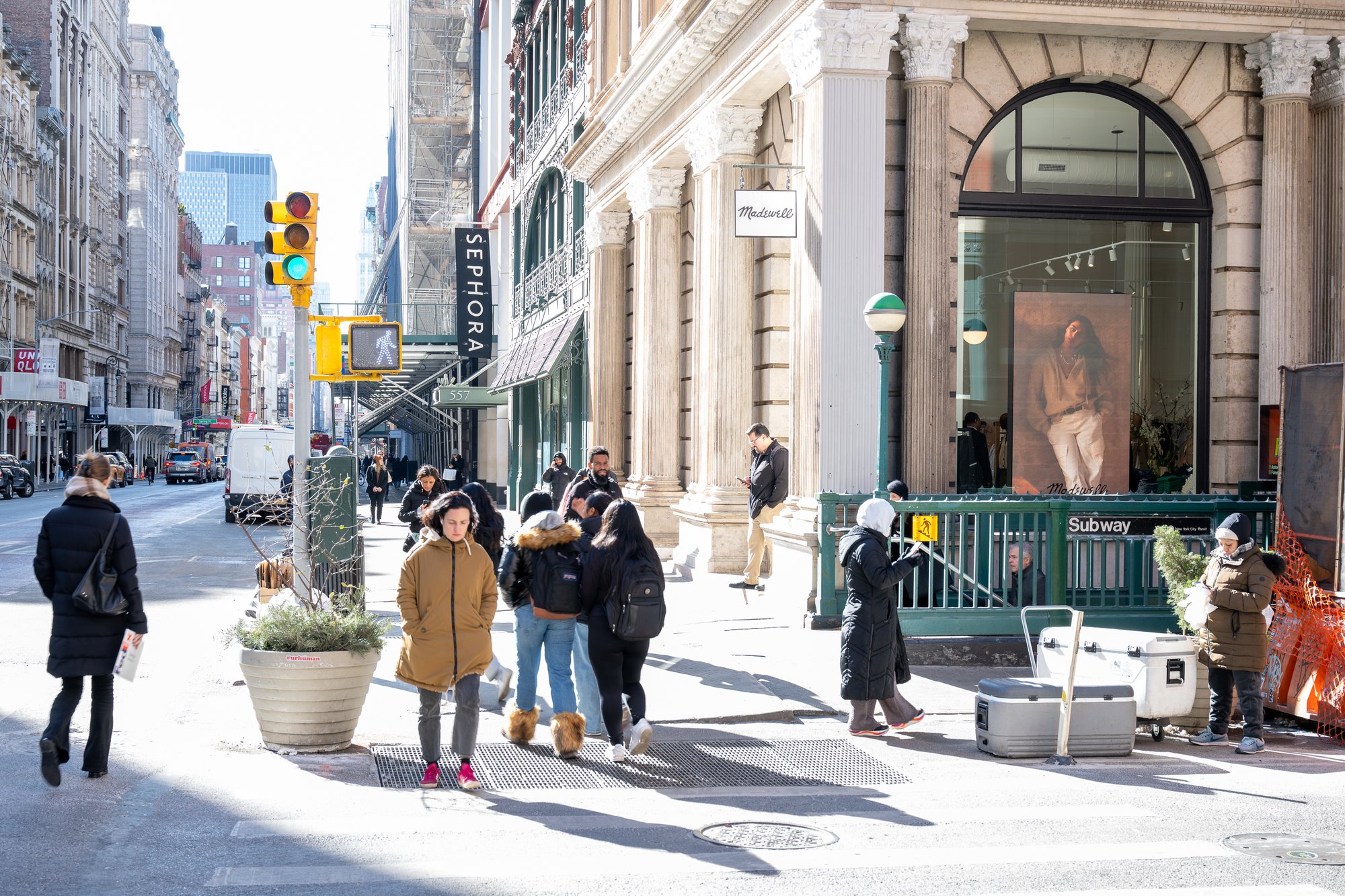 People walking on a city sidewalk in front of shops.