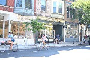 Person biking past shops on a city street.