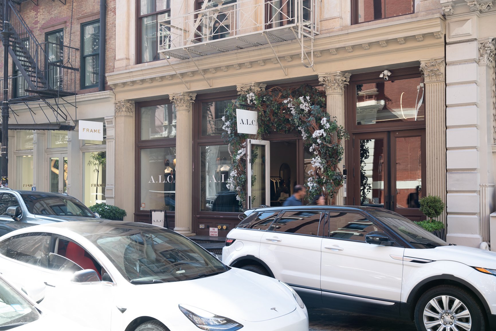A storefront with a floral archway and two cars parked in front.