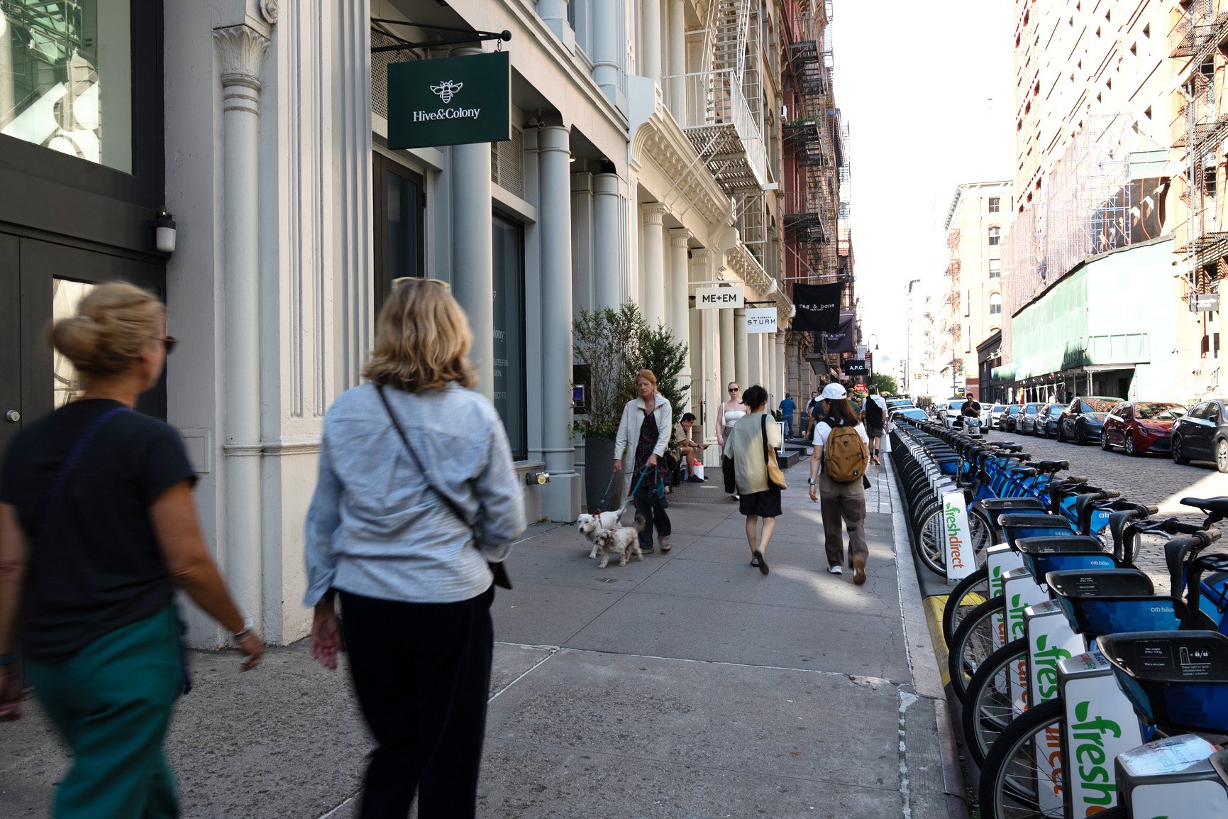 People walking down a city street with shops and parked bikes.