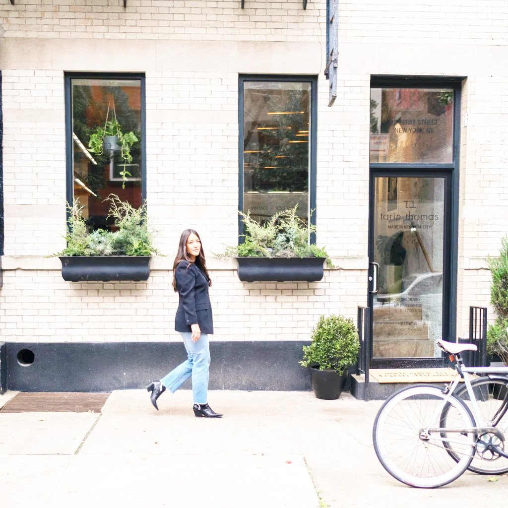 Woman walking past a building with plants and a bicycle.