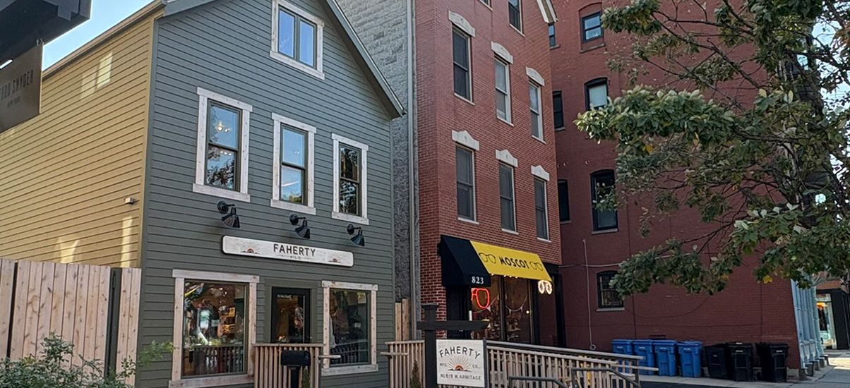 Two men standing outside a cafe, a bicycle, and city buildings in the background.