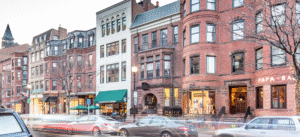 Three-story white building with green awning between brick buildings on a city street.