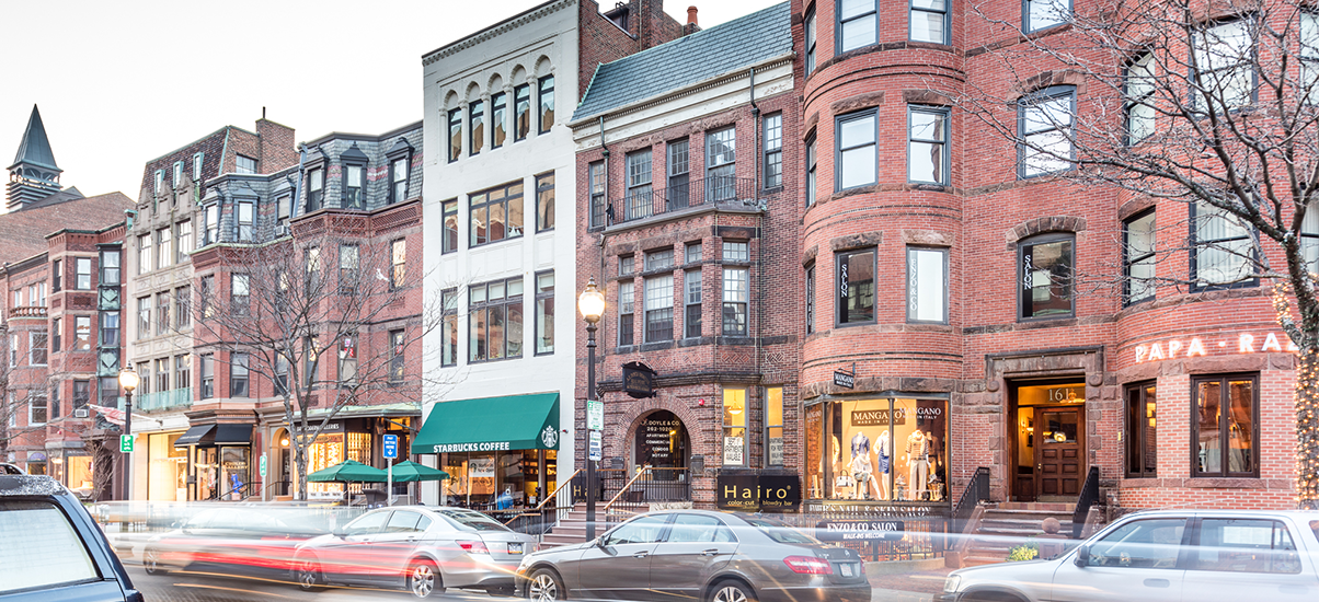 Three-story white building with green awning between brick buildings on a city street.