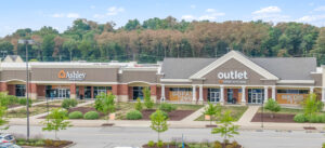 Aerial view of a shopping center with parking lot and surrounding trees.