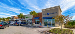Shopping center parking lot under a bright blue sky.
