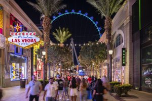 Night view of a Las Vegas street with a Ferris wheel in the background.