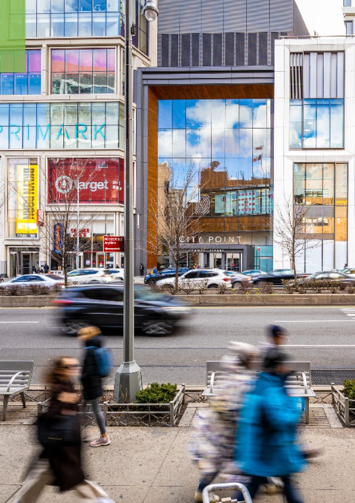 Modern city street with blurred pedestrians and cars passing storefronts.